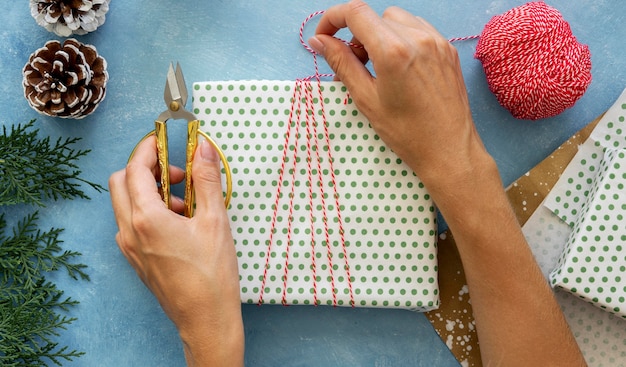 Vista superior de mãos envolvendo um cordão em volta do presente de natal