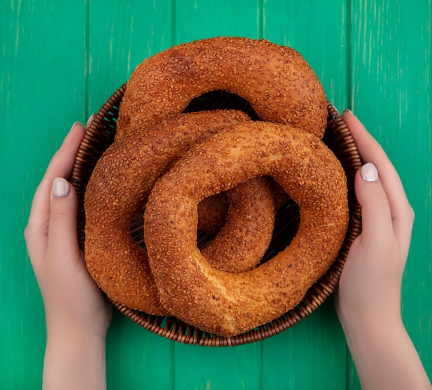 Vista superior de mãos femininas segurando um balde com o tradicional bagel turco em um fundo verde de madeira