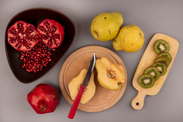 Vista superior de marmelos frescos cortados ao meio em uma placa de cozinha de madeira com romãs em uma tigela com fatias de kiwi em uma placa de cozinha de madeira