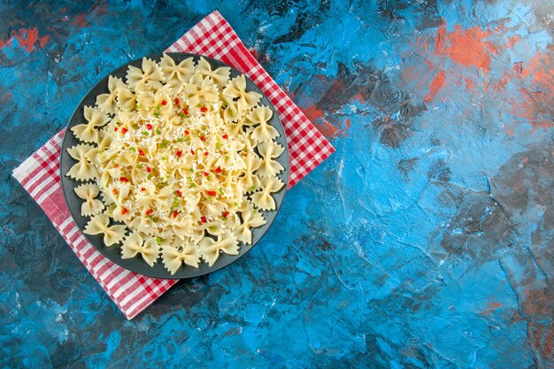 Vista superior de massa farfalle italiana crua com legumes em uma toalha vermelha despojada do lado direito na mesa azul