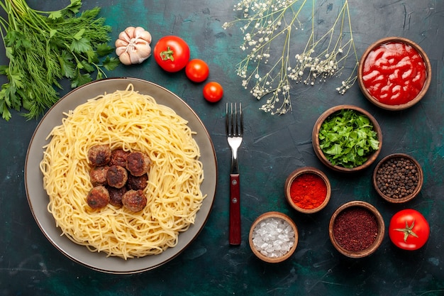 Vista superior de massas italianas cozidas com almôndegas, temperos e verduras na mesa azul escura