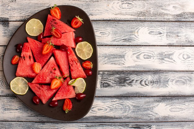 Vista superior de melancia fatiada com morango em fatias de limão na superfície cinza