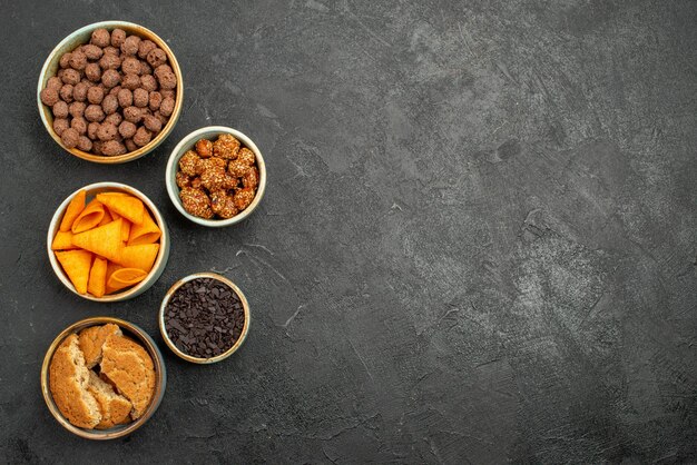 Vista superior de nozes e batatas fritas dentro de pequenos potes em chips de salgadinhos cinza-escuro de mesa