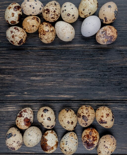 Vista superior de ovos de codorna com conchas de cor creme com manchas marrons, dispostas em fundo de madeira com espaço de cópia