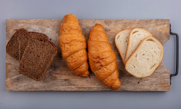 Vista superior de pães como croissant fatiado de centeio e baguete em uma tábua em fundo cinza