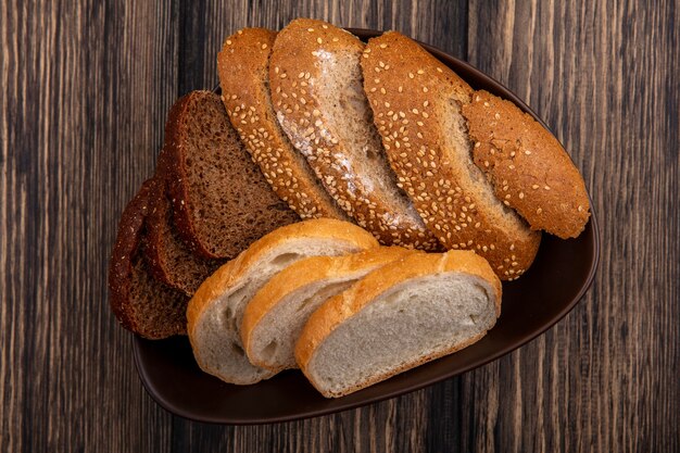 Vista superior de pães como fatias de centeio-espiga marrom e outras brancas em uma tigela com fundo de madeira