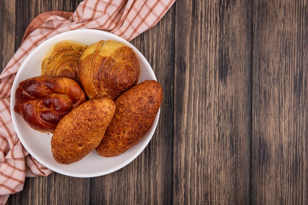 Foto grátis vista superior de pães em um prato em um pano xadrez em um fundo de madeira com espaço de cópia