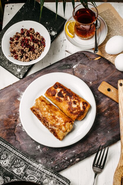 Vista superior de panqueca frita rola servido com chá no copo armudu em uma mesa de madeira