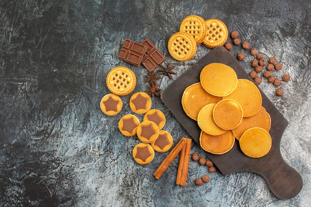 Vista superior de panquecas em uma bandeja de madeira com biscoitos e doces em um fundo cinza