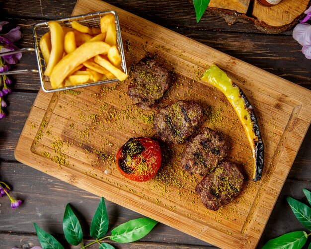 Vista superior de pedaços de bife de cordeiro, servido com batatas fritas, pimenta e tomate grelhado