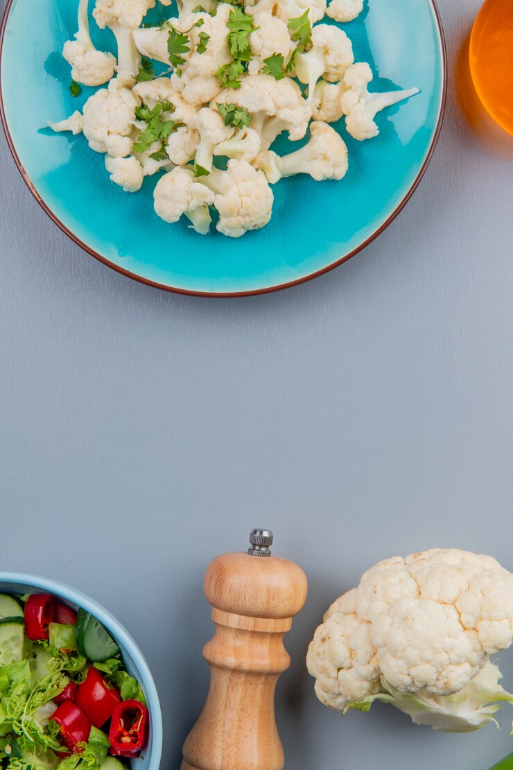 Foto grátis vista superior de pedaços de couve-flor com coentro no prato e manteiga de sal e salada de legumes em fundo azul