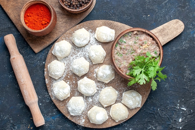 Vista superior de pedaços de massa enfarinhada com verduras de carne picada junto com pimenta no escuro, massa comida carne crua massa jantar