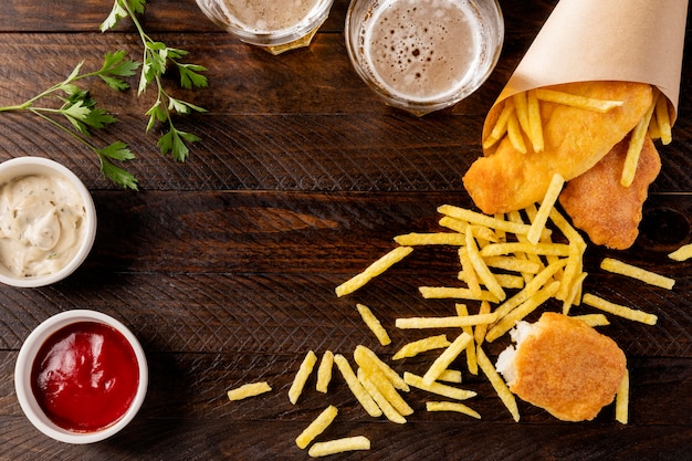 Vista superior de peixe e batatas fritas em cone de papel com cerveja
