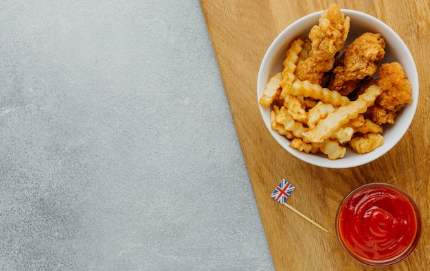 Vista superior de peixe e batatas fritas em uma tigela com ketchup e copie o espaço