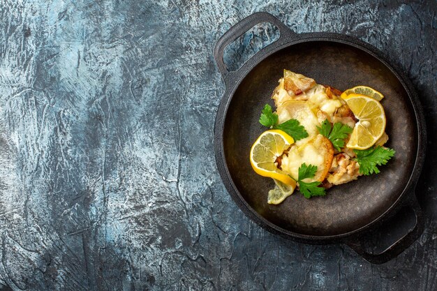 Vista superior de peixe frito na panela com limão e salsa em fundo cinza