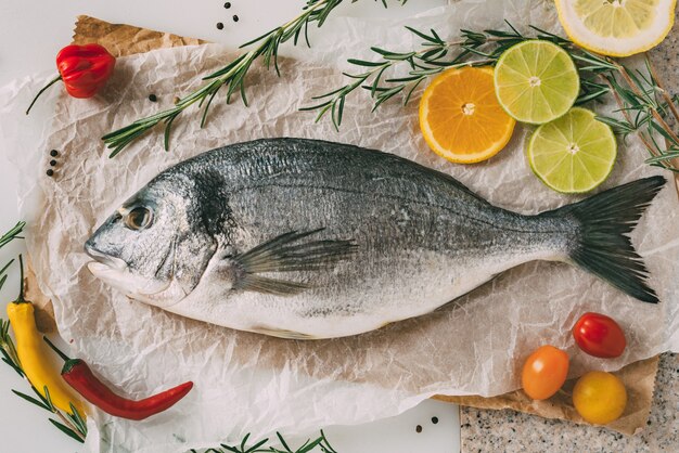 Vista superior de peixes dourados na assadeira com alecrim, limão, laranja e tomate