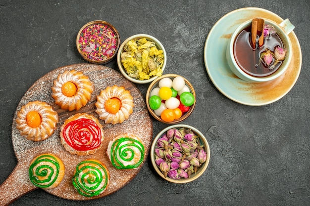 Vista superior de pequenos bolos deliciosos com chá de doces e flores em preto