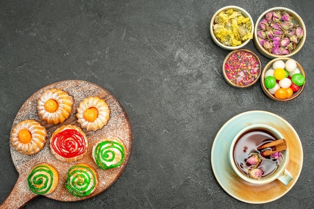 Vista superior de pequenos bolos deliciosos com chá de doces e flores em preto