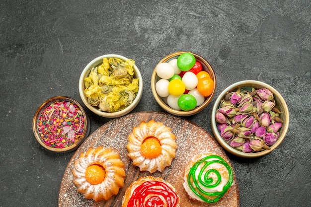 Vista superior de pequenos bolos deliciosos com doces e flores em preto