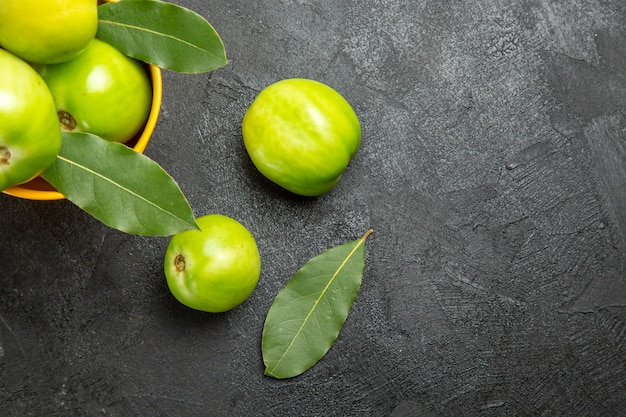 Vista superior de perto balde de tomates verdes e folhas de louro e tomates na mesa escura com espaço de cópia