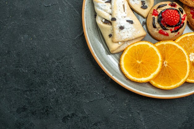 Vista superior de perto biscoitos saborosos com bolos de frutas e fatias de laranja na superfície escura frutas bolo doce torta chá açúcar