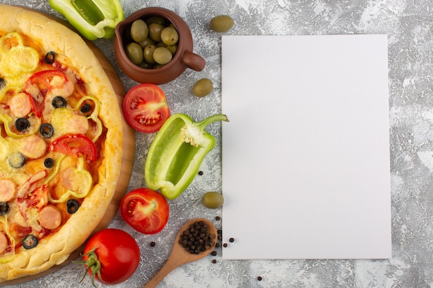 Vista superior de perto deliciosa pizza de queijo com salsichas de azeitonas e tomates na mesa cinza com refeição de massa italiana fast-food de papel em branco