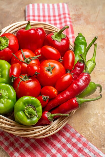 Vista superior de perto pimentas verdes e vermelhas pimentas tomates em cesta de vime toalha de cozinha em fundo âmbar