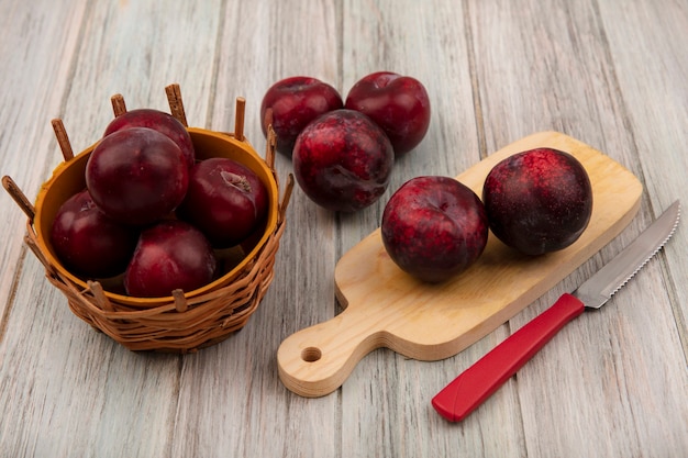 Vista superior de pluots frescos isolados em uma placa de cozinha de madeira com uma faca com pluots em um balde em uma parede de madeira cinza