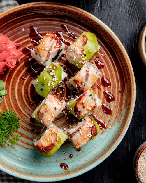 Vista superior de rolos de sushi com enguia abacate e pepino com gengibre e wasabi em um prato na madeira