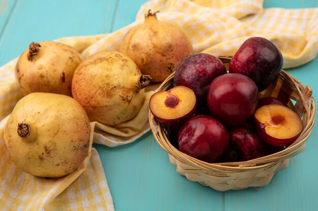 Vista superior de romãs amarelas isoladas em um pano xadrez amarelo com pluots em um balde em uma superfície de madeira azul