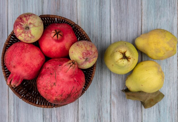 Vista superior de romãs frescas e saudáveis em um balde com maçãs e marmelos em um fundo cinza