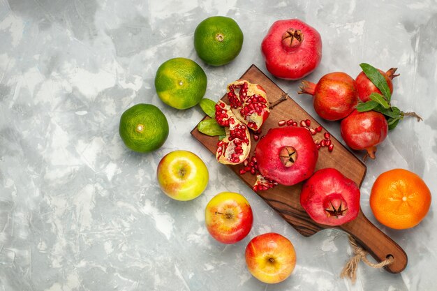 Vista superior de romãs vermelhas frescas com tangerinas e maçãs na mesa branca