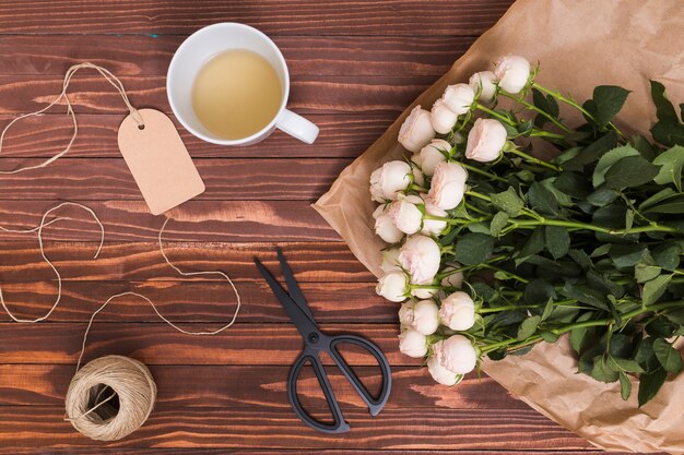 Vista superior de rosas brancas; chá de limão; corda e tesoura; etiqueta de preço acima do pano de fundo texturizado de madeira
