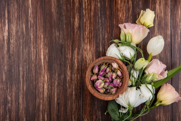 Vista superior de rosas frescas com botões de rosa em uma tigela de madeira sobre um fundo de madeira com espaço de cópia