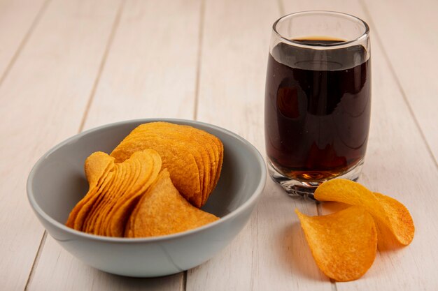 Vista superior de saborosas batatas fritas crocantes em uma tigela com um copo de coca-cola em uma mesa de madeira bege