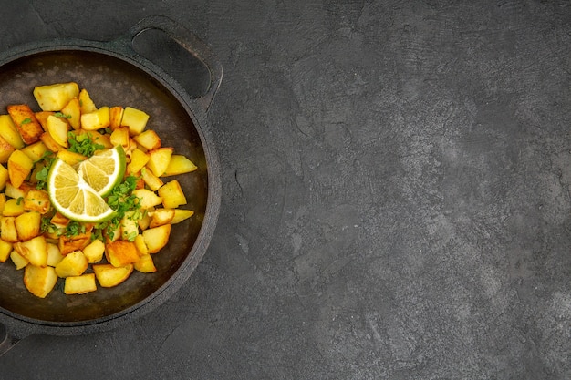 Vista superior de saborosas batatas fritas dentro de uma panela com rodelas de limão na superfície escura