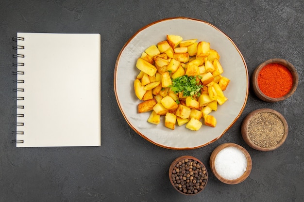 Vista superior de saborosas batatas fritas dentro do prato com temperos na superfície escura