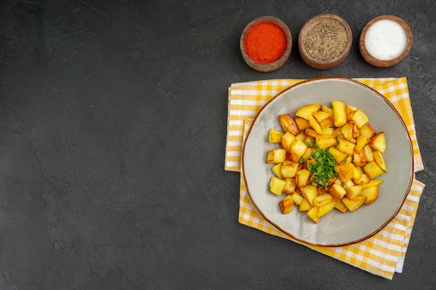 Vista superior de saborosas batatas fritas dentro do prato com temperos na superfície escura