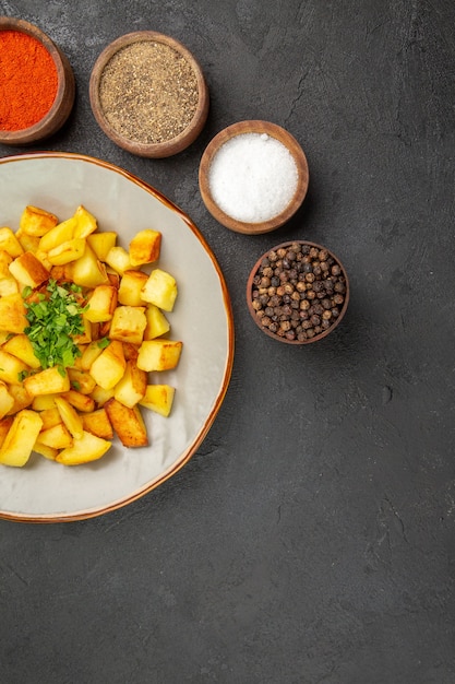 Foto grátis vista superior de saborosas batatas fritas dentro do prato com temperos na superfície escura