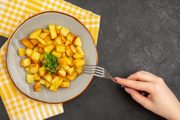 Vista superior de saborosas batatas fritas dentro do prato com verduras na superfície cinza-escura