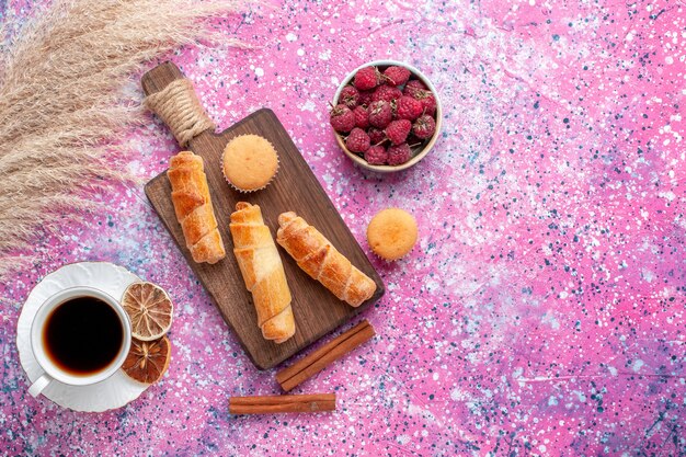 Vista superior de saborosas framboesas frescas dentro de um prato branco com pãezinhos de chá e canela na superfície rosa