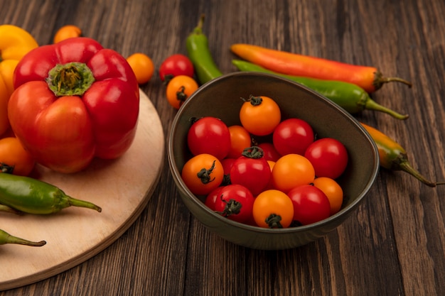 Vista superior de saborosas pimentas em uma placa de cozinha de madeira com tomate cereja em uma tigela na parede de madeira