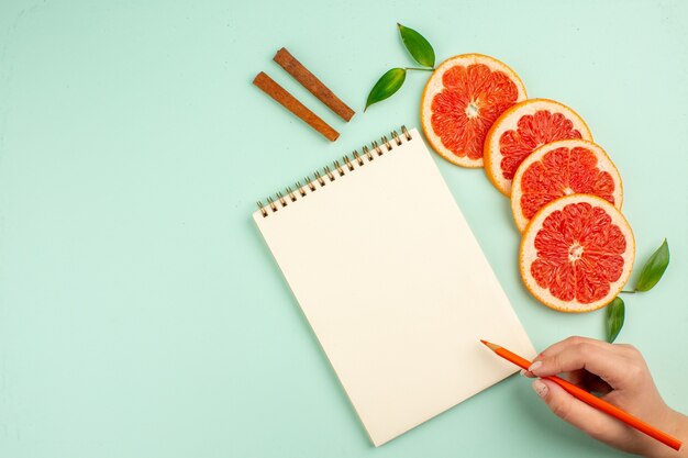 Vista superior de saborosas toranjas frescas com bloco de notas na superfície azul-clara