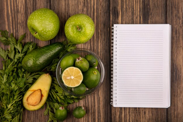 Vista superior de saborosos feijoas maduros com limão em uma tigela de vidro com maçãs verdes, abacate, feijoas e salsa, isolado em um fundo de madeira com espaço de cópia