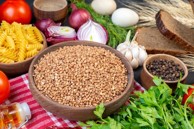 Vista superior de sêmolas de buchwheat na toalha vermelha despojada massas vegetais frescos fatias de pão garrafa de óleo caída um pacote verde na mesa preta