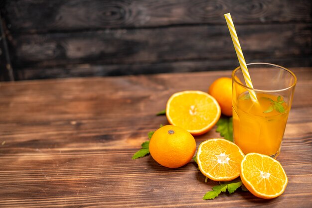 Vista superior de suco de laranja fresco em um copo servido com tubo de hortelã e laranjas inteiras cortadas no lado esquerdo em uma mesa de madeira