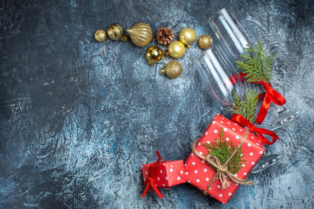 Vista superior de taças de vidro caídas e conjunto de talheres, caixa de presente de acessórios de decoração e meia de natal no lado esquerdo na mesa escura