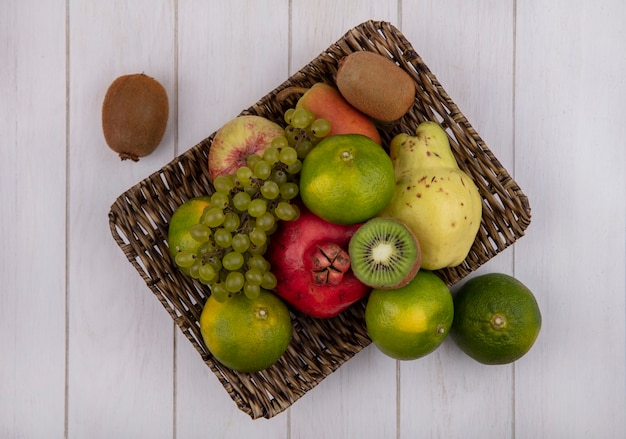 Vista superior de tangerinas com uvas de romã, pêra, maçã e kiwi em uma cesta