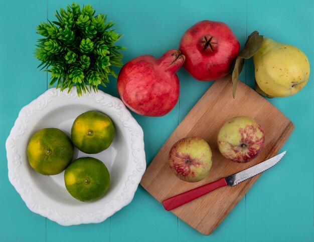 Vista superior de tangerinas em um prato com maçãs em uma tábua de cortar e romãs com pêra