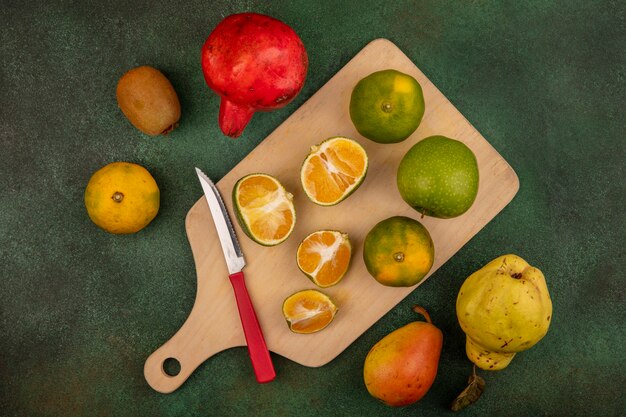 Vista superior de tangerinas frescas em uma placa de cozinha de madeira com uma faca com frutas deliciosas, como a romã-pera